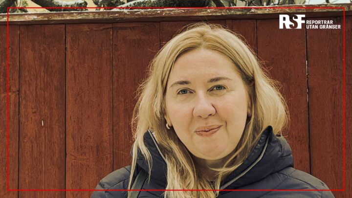 Oksana Romaniuk, chef för Institute of Mass Information (IMI), framför ett rött träplank med Reportrar utan gränsers logotyp i bildens övre högra hörn.