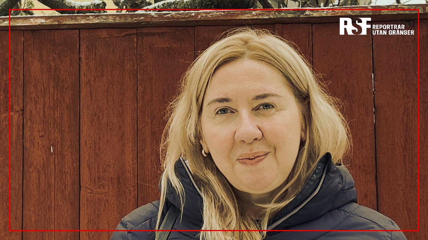Oksana Romaniuk, chef för Institute of Mass Information (IMI), framför ett rött träplank med Reportrar utan gränsers logotyp i bildens övre högra hörn.