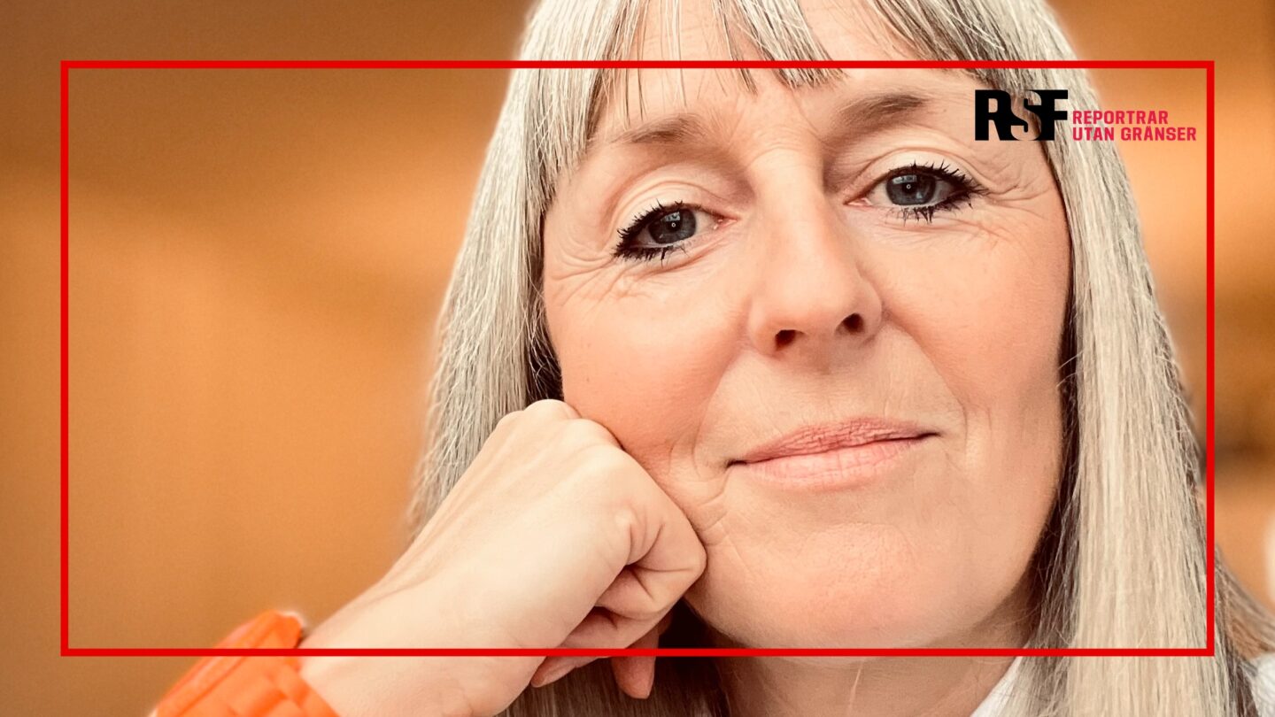 Närbild av Sara med grått hår som vilar huvudet mot handen, mot en varm orange bakgrund, med en röd ram och Reportrar utan gränsers logo i hörnet.